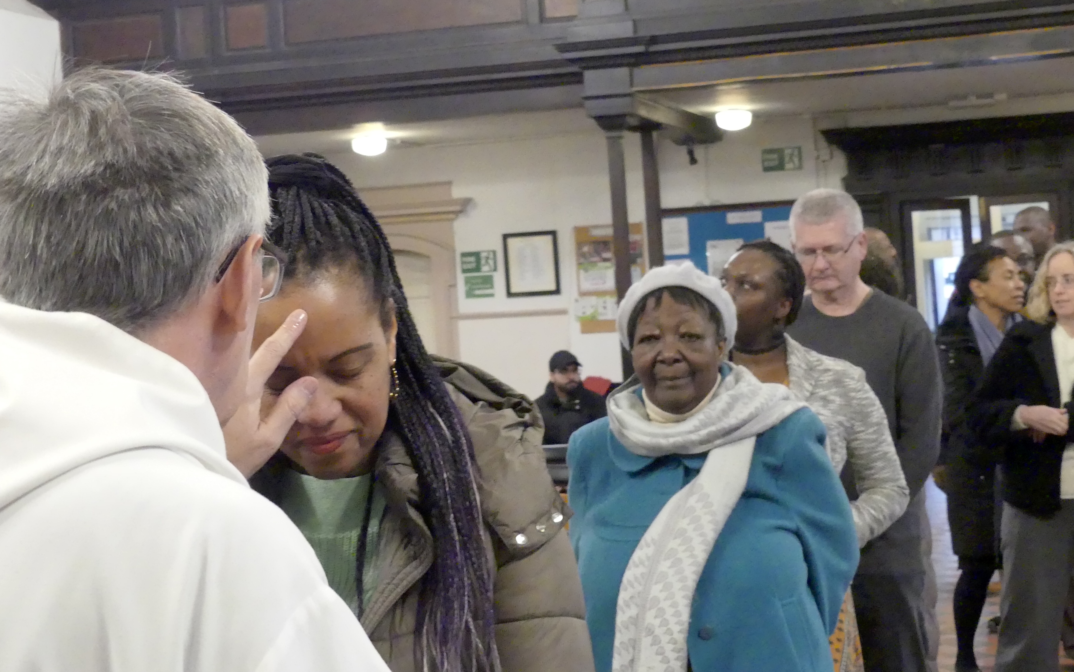 People stand in line and Bishop Simon anoints the head of a lady with oil