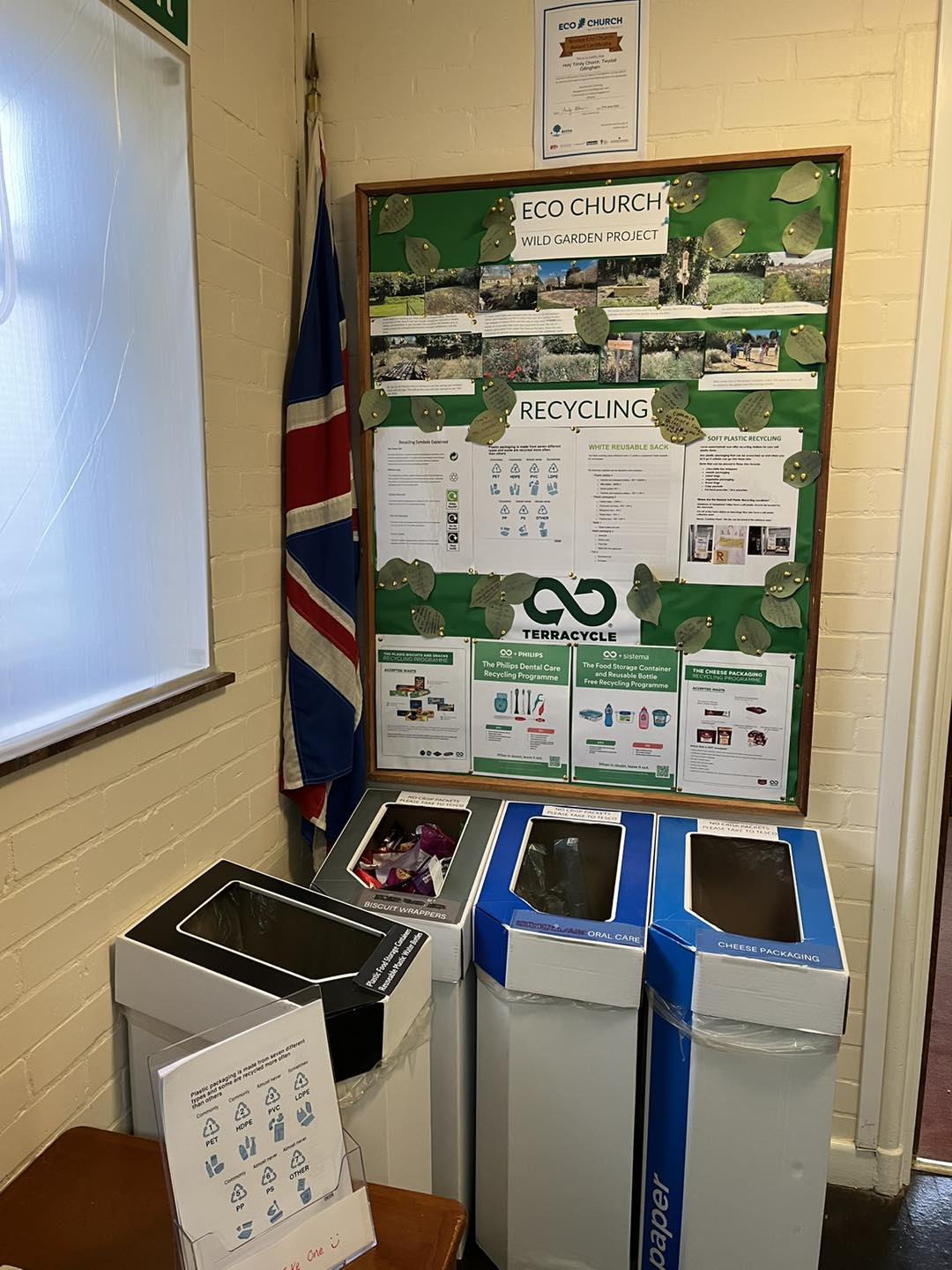 A noticeboard with recycling information on it sits above three recycling bins