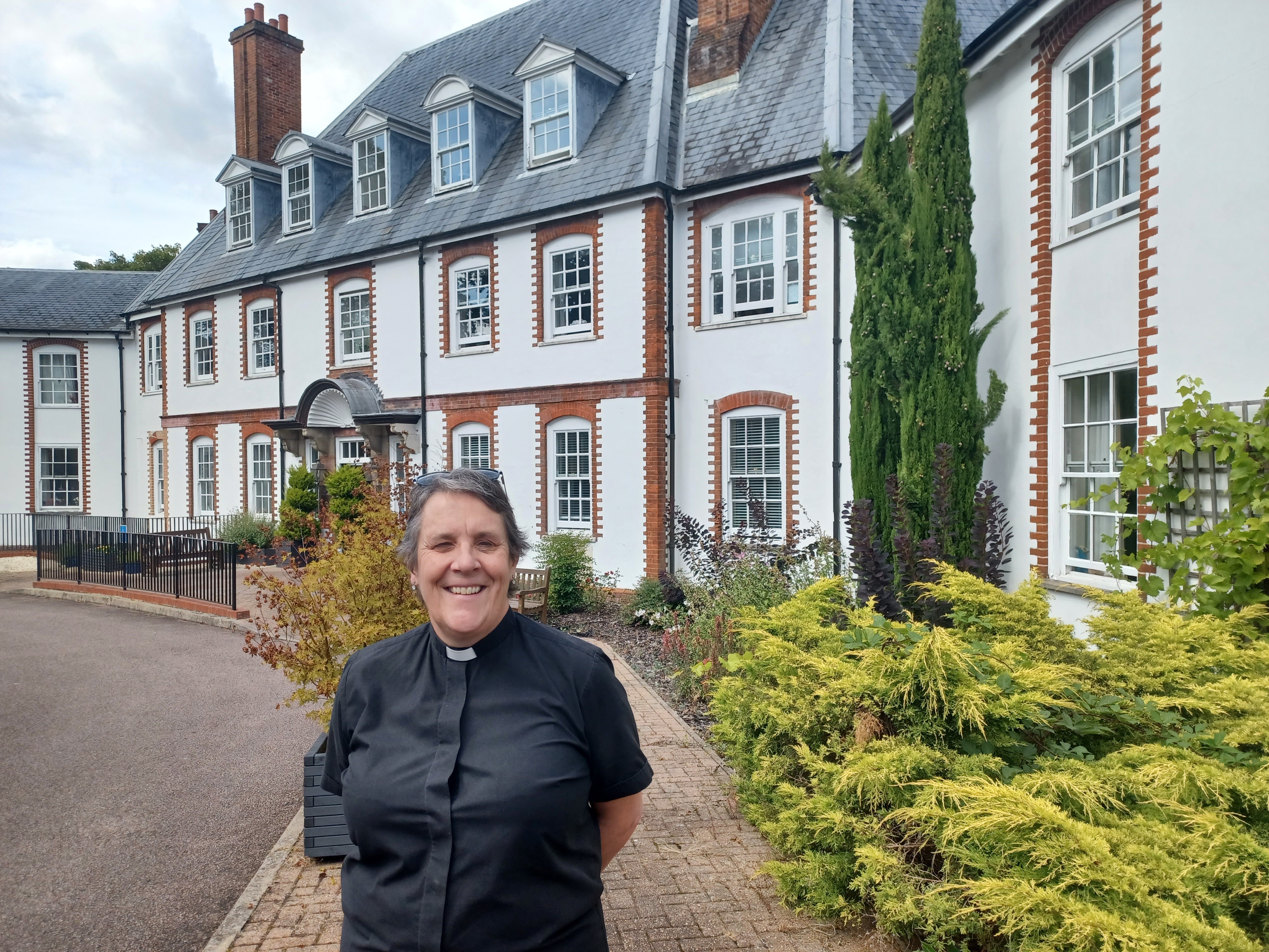 The Rev Anne Bourne stands outside a pleasant white painted building