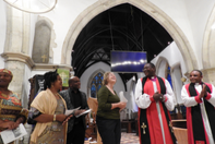 A group stands smiling in a church, they include two bishops from Mpwapwa and Konda, as well as local members of the church in Kent