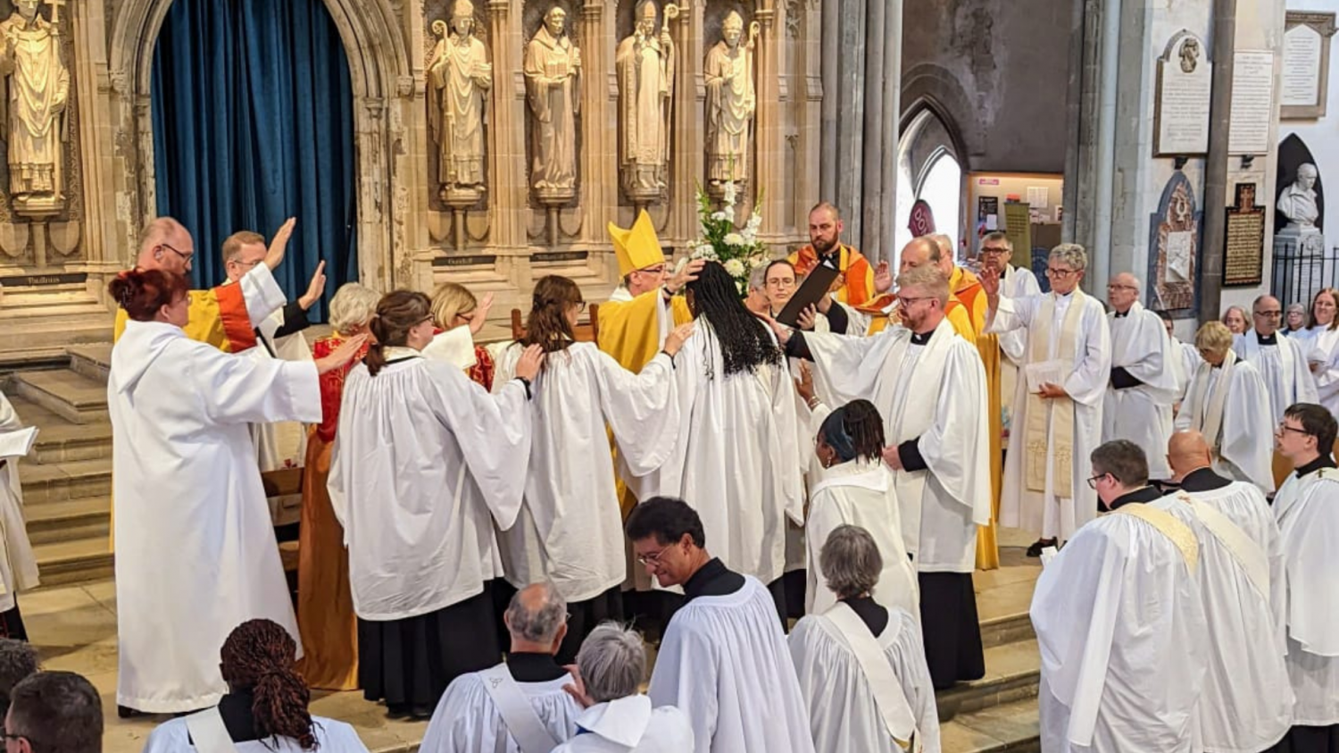 The bishop lays his hands on the head of the ordinand. Other supporting clergy gather around the candidate and raise their hands above the ordinand.