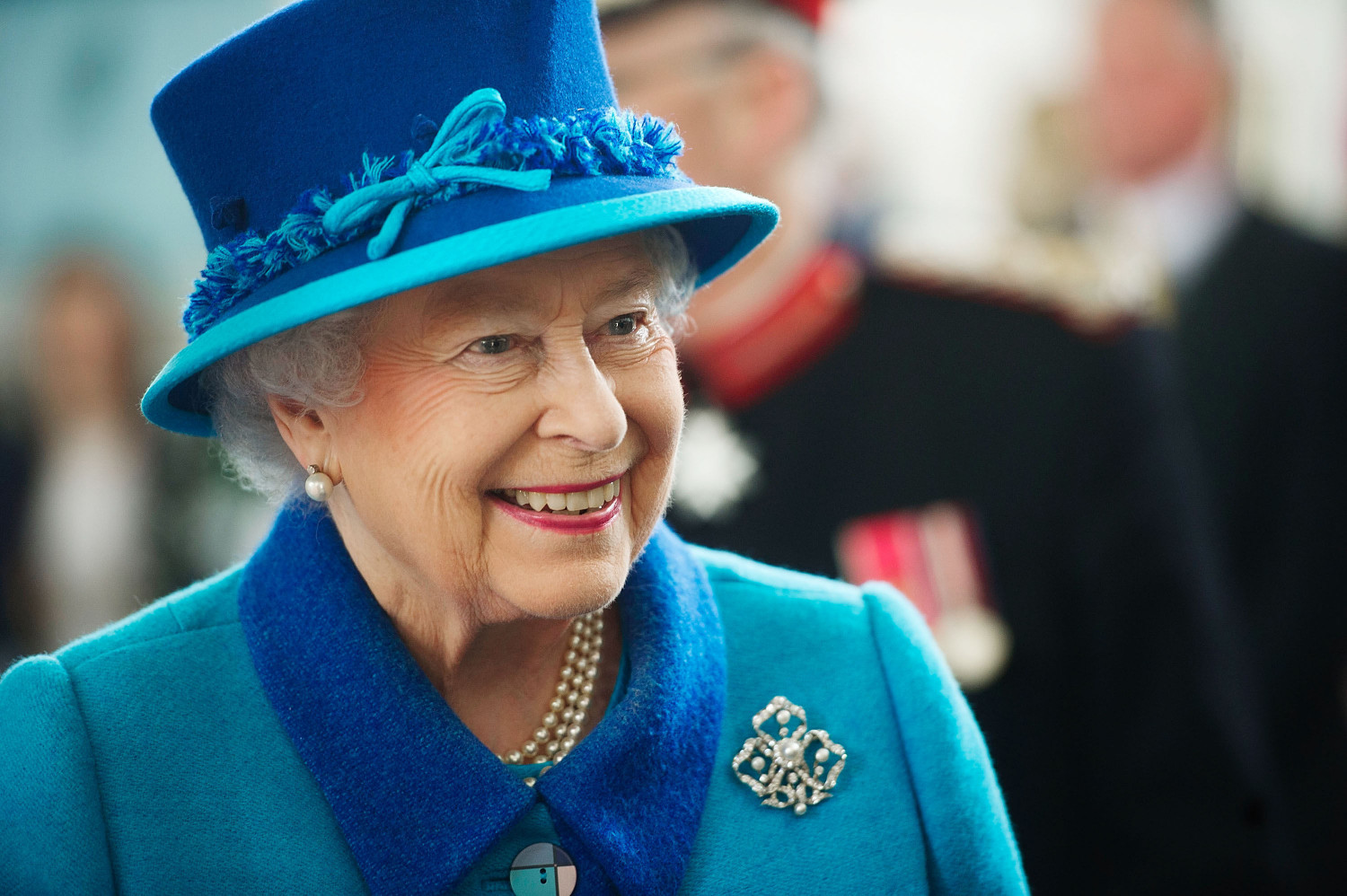 A close up photo of The Queen in later life, dressed in blue and smiling. 