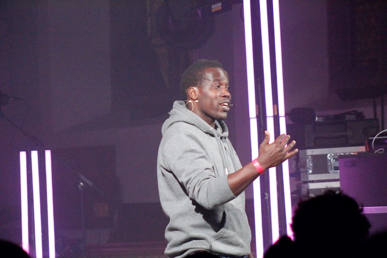 Surrounded by the purple glow of neon lights, the Reverend Dennis Adide addresses the young people.